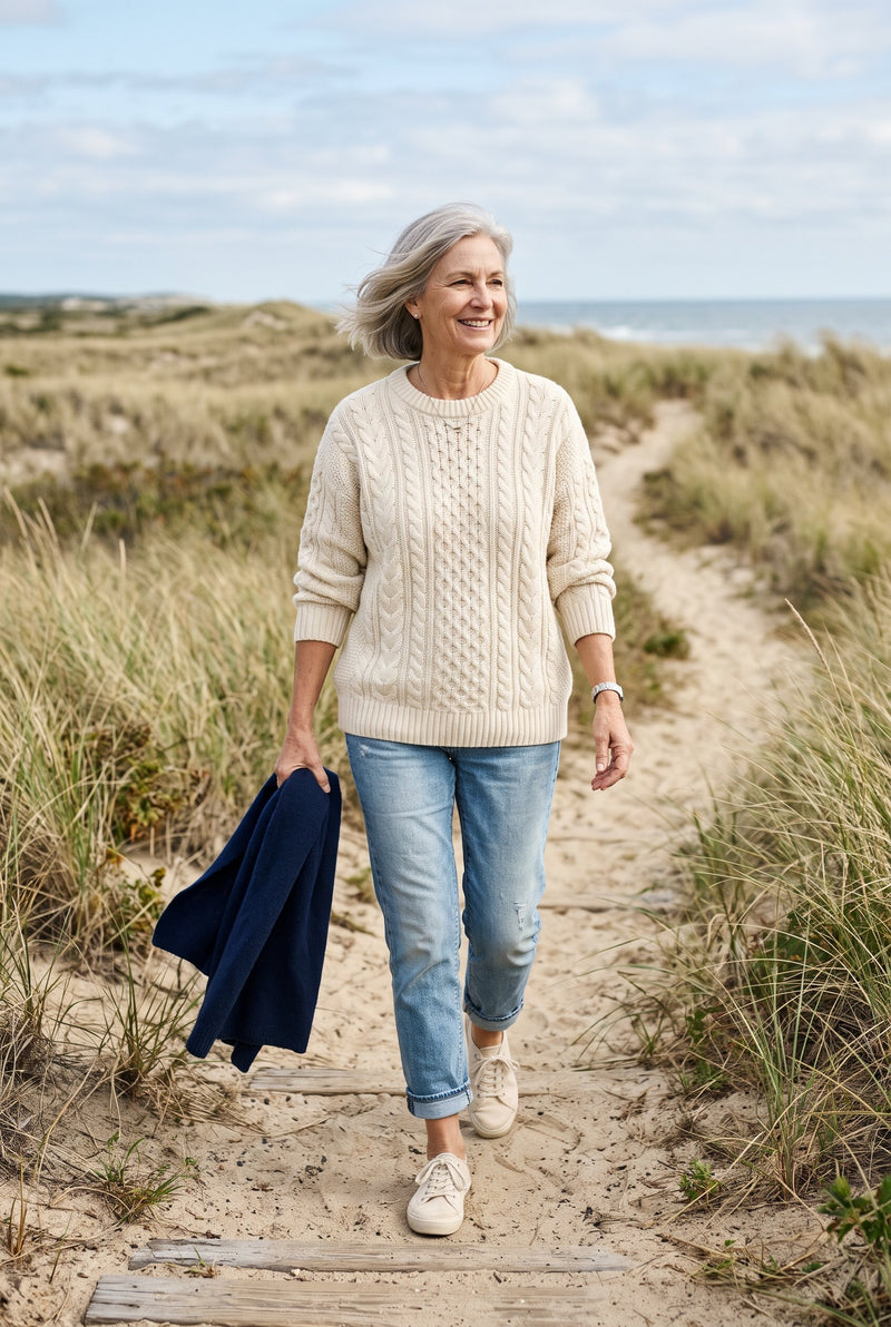A woman in a cream cable-knit sweater on a sandy path between the dunes