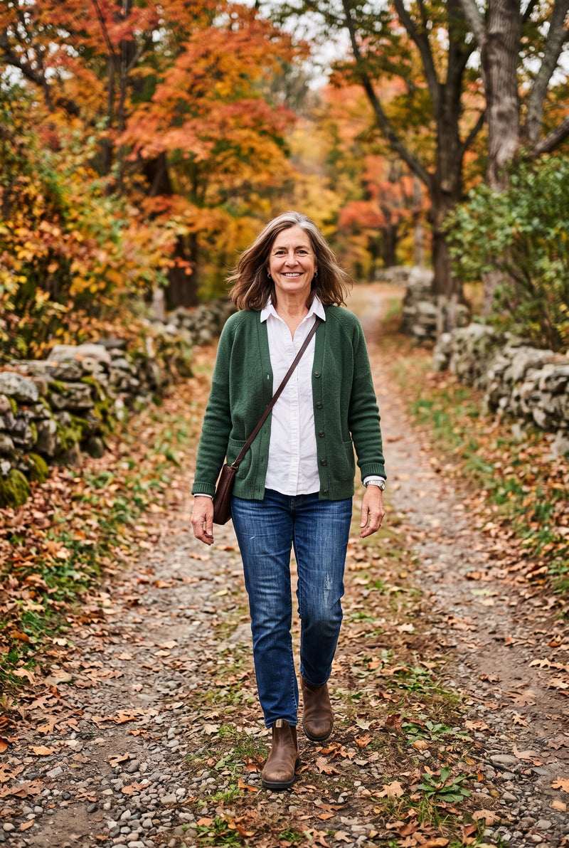 A woman in a green cardigan and jeans walking down a country lane in autumn