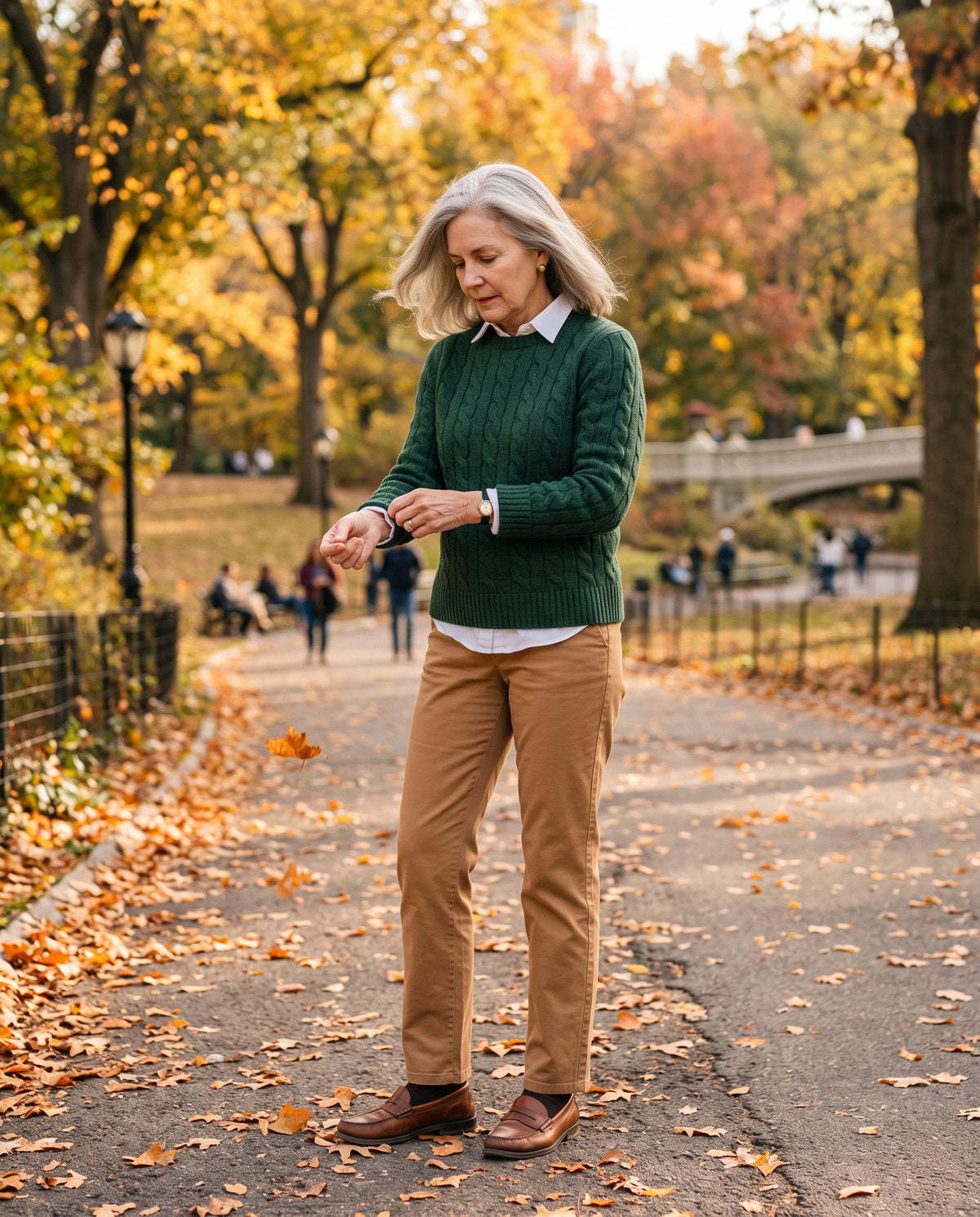 A woman in a green cable-knit sweater and camel trousers in a park in autumn